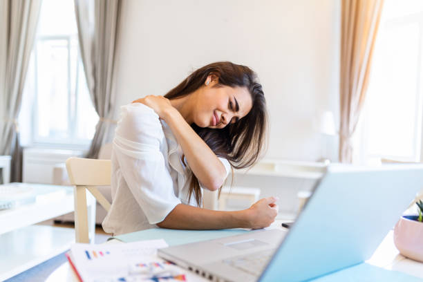 porträt einer jungen gestressten frau, die am schreibtisch des home office vor dem laptop sitzt, schmerzenden hals mit schmerzverzerrtem ausdruck berührt, nach der arbeit am laptop unter nackenschmerzen leidet - overworked worried distraught front view stock-fotos und bilder