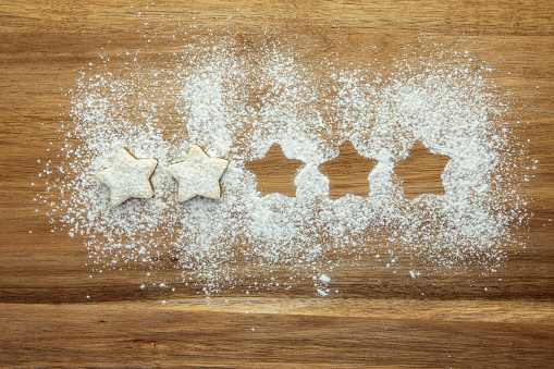 A row of stars made by pastry stars and negative stencil shapes in icing sugar on a wooden board viewed directly above with copy space. Part of a series.