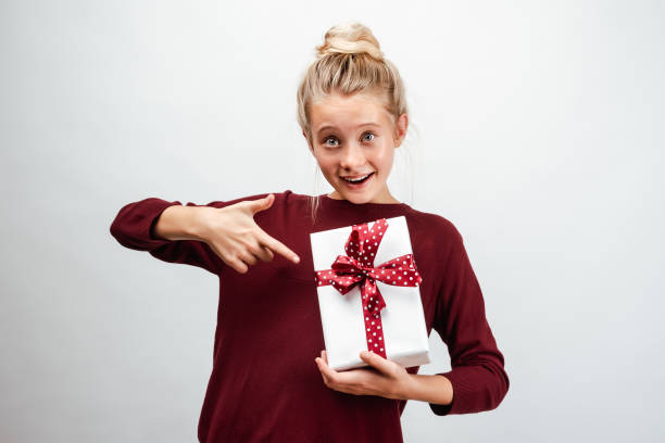 bella ragazza bionda di 10-12 anni vestita con maglione casual, con in mano una confezione regalo - 10 11 years cheerful happiness fun foto e immagini stock