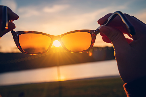 Hands holding sunglasses on a beach at sunset