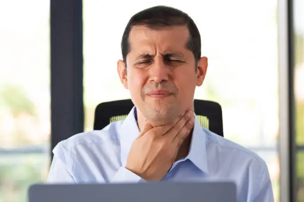 Shot of a young businessman experiencing throat pain while working in an office