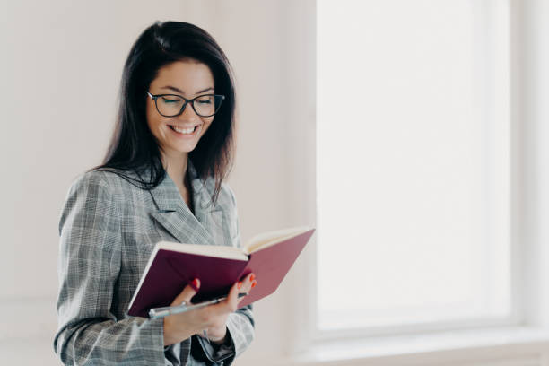 istock Satisfied brunette woman has happy expression writes down working plan in notepad has red manicure formal clothes records information for organization process wears spectacles notes financial schedule 1271094071