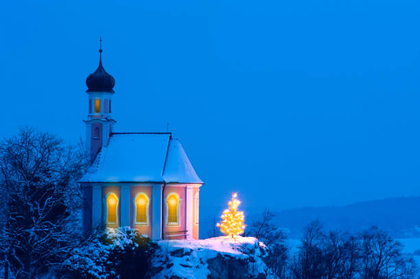 istock romantic Christmas chapel with illuminated tree in snow on hill 1271095666