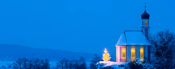 istock romantic Christmas chapel with illuminated tree in snow on hill 1271095723