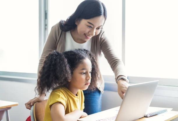 istock Happy Asian female teacher helping school kids using laptop computers in IT class. Education, elementary school, learning and technology concept. 1271099322