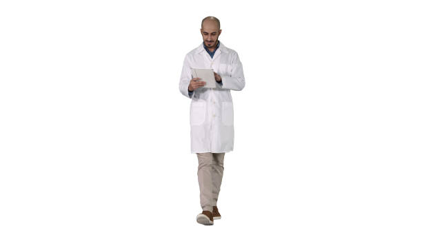 istock Mature male doctor holding digital tablet using it and walking on white background 1271099342