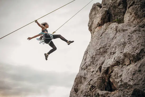 One young woman, free climber, rappelling down a cliff in the mountains.