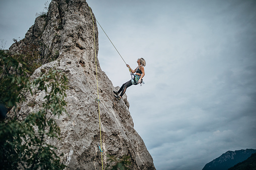 One young woman, free climber, climbing on the mountain equipped with climbing gear.