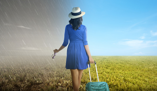 Asian woman with suitcase standing on the meadow field with a different climate. Concept of changing the environment