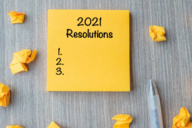 istock 2021 RESOLUTIONS word on yellow note with pen and crumbled paper on wooden table background. New start, Strategy and Goal concept 1271111956