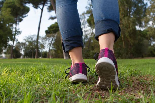 istock Woman with sneakers and jeans walking on grass 1271112100