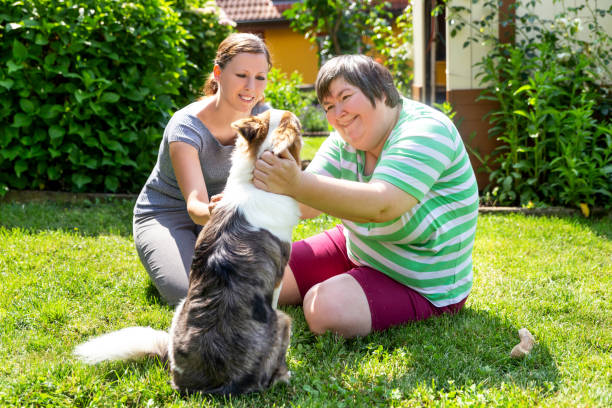 mujer mentalmente discapacitada con una segunda mujer y un perro de compañía, concepto de aprendizaje por vida asistida animal - disabled adult fotografías e imágenes de stock