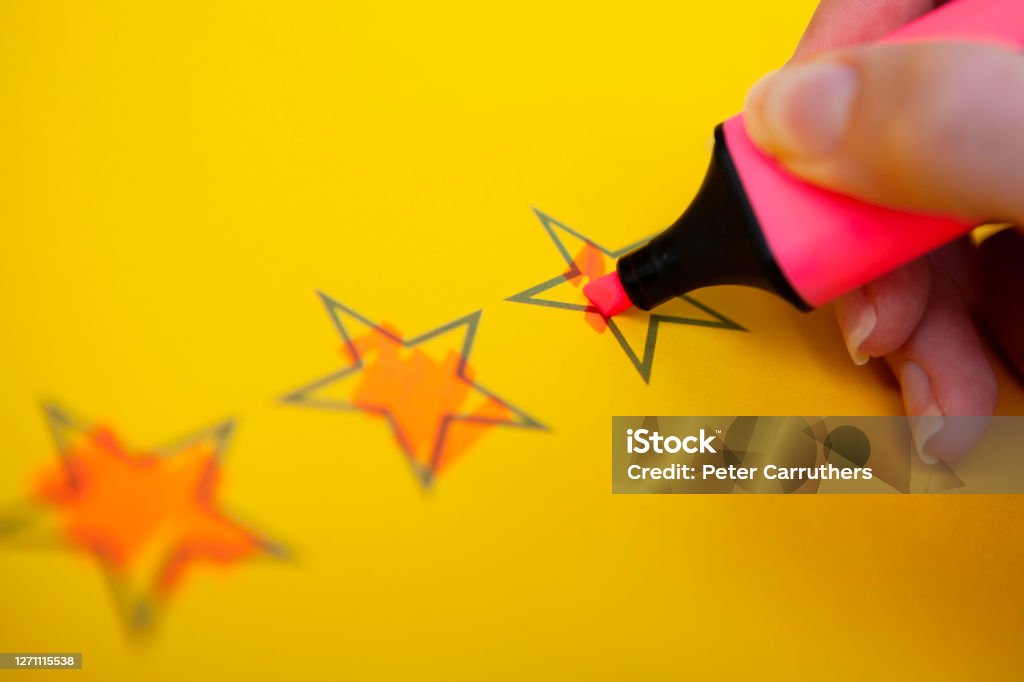 Hand holding highlighter and colouring rating stars Close-up of a hand holding a pink highlighter pen colouring in rating stars on yellow paper with copy space Customer Experience Stock Photo
