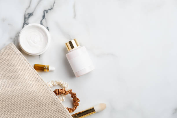Makeup bag with natural cosmetic products set on marble desk. Flat lay, top view moisturizer cream, body lotion, serum dropper bottle, make-up brush. Skincare concept.