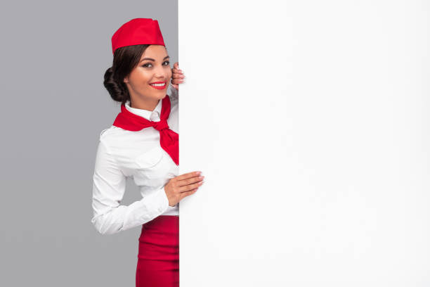 cheerful air hostess peeking out from behind blank banner - color image people air vehicle airplane imagens e fotografias de stock