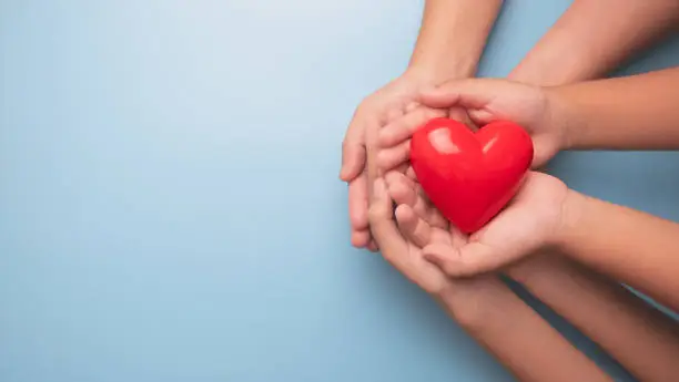 Photo of Hands holding a red heart on blue background, CSR or Corporate Social Responsibility, health care, family insurance