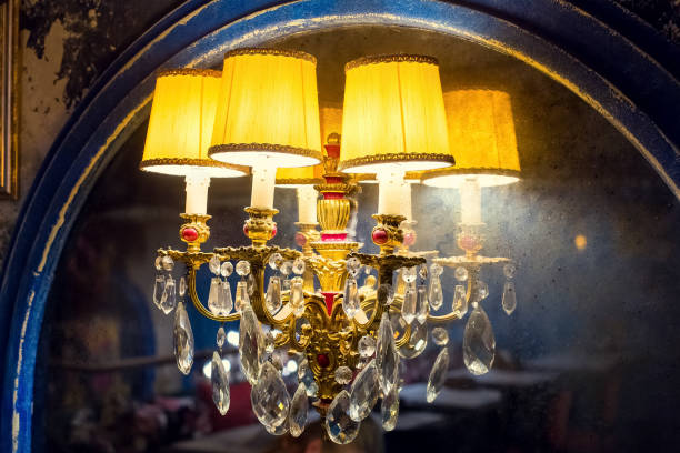 istock a candelabrum with a yellow lampshade with glass elements on an old mirror with a worn blue wooden frame, a wall lamp in a dark retro interior shines with warm light closeup side view, nobody. 1271128315