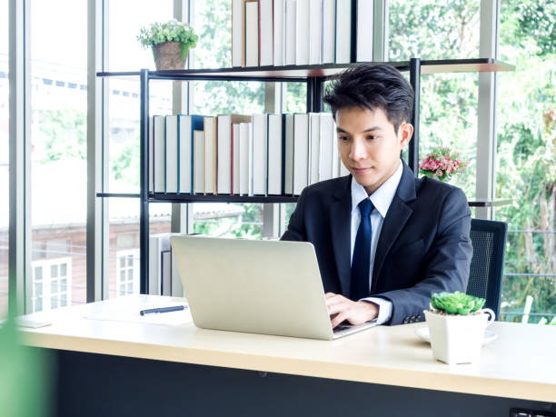 istock Young Asian businessman in suit working with laptop computer in office. 1271130120