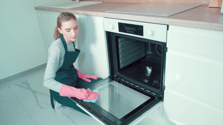 The girl professional cleaner wipes the door inside with a rag of the oven.