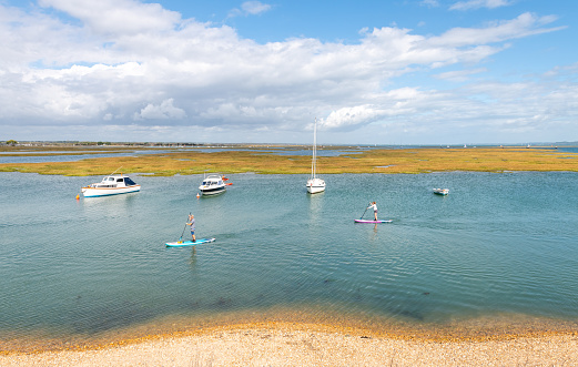 Keyhaven, UK. Sunday 6 September 2020. People paddleboarding on Keyhaven Water in Hampshire with other boats moored.