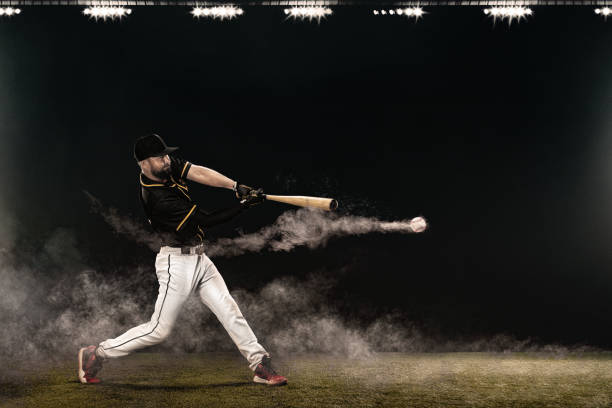Baseball player with bat taking a swing on grand arena. Ballplayer on dark background in action. stock photo