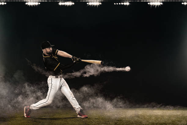Baseball player with bat taking a swing on grand arena. Ballplayer on dark background in action. Porfessional baseball player with bat taking a swing on grand arena. Ballplayer on stadium in action swinging stock pictures, royalty-free photos & images