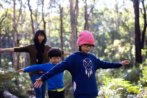 Front view of mother and daughter with arms outstretched walking on log in Boranup Forest Maze, Western Australia.