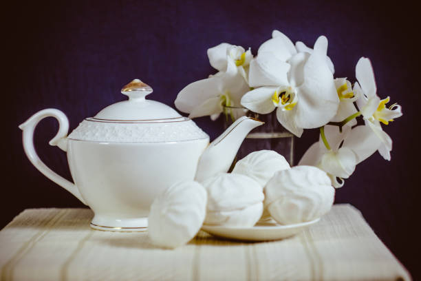 Black and white still life with a tea kettle, a branch of a blooming orchid and marshmallows