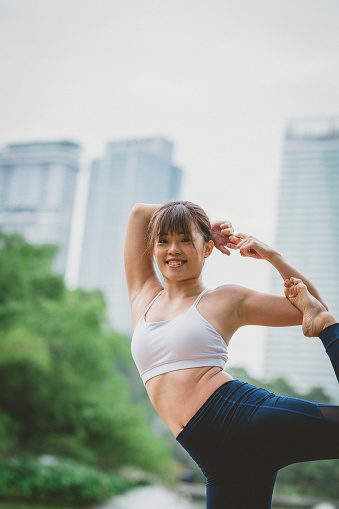 An Asian woman doing Natarajasana exercise and relax with sportswear in city public park. Concept of Meditation, Relaxation and Healthy lifestyle.