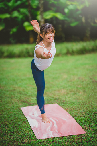 Fitness Asian woman doing Natarajasana exercise and relax with sportswear on grass in public park. Concept of Meditation, Relaxation and Healthy lifestyle.