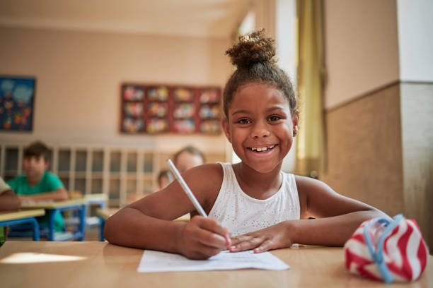 istock Beautiful cheerful child in a classroom writing on a test 1271141987