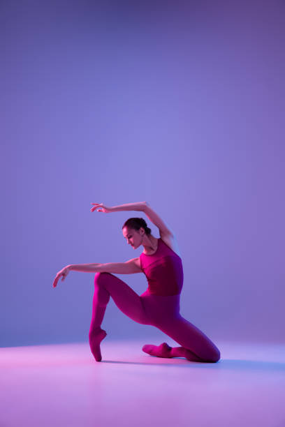 Young and graceful ballet dancer isolated on purple studio background in neon light