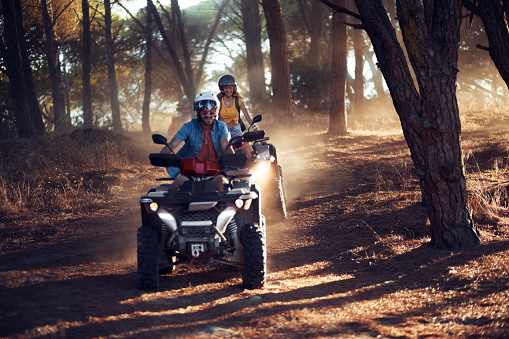 Two young friends wearing helmets having fun and riding quad bikes together in the forest