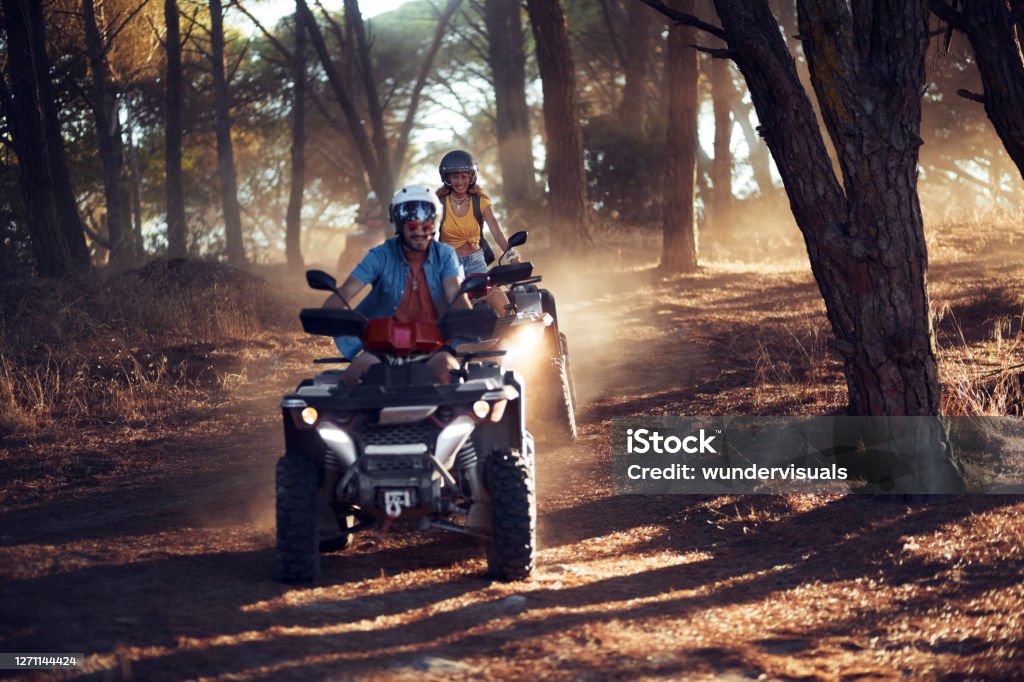 Two friends wearing helmets having fun and riding quad bikes together in the forest Two young friends wearing helmets having fun and riding quad bikes together in the forest Quadbike Stock Photo