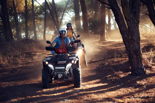 Photo of Two friends wearing helmets having fun and riding quad bikes together in the forest