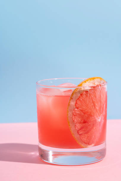 cóctel de pomelo sobre mesa rosa y bebida de verano de pared azul - pomelo fotografías e imágenes de stock