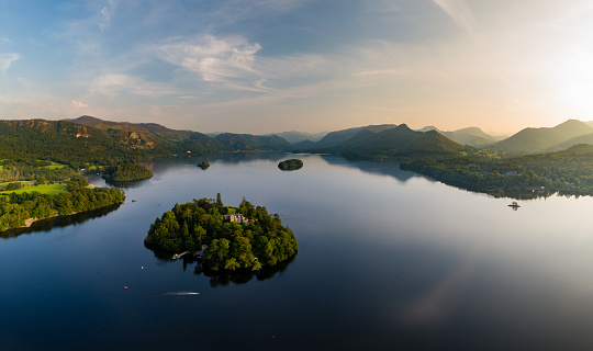 Aerial panorama of sunset next to a beautiful, flat calm lake surrounded by hills (Derwent Water, Keswick, England)