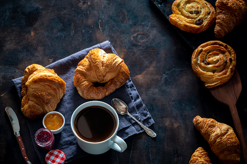 Coffee breakfast with pastries croissants, butter, cheesecake homemade on dark background