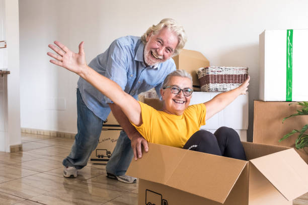 happiness of two senior people in empty room playing like children in relocation happy for new beginning like retired with moving boxes on the floor - independence imagens e fotografias de stock