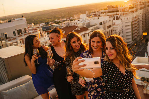 Group of young friends taking a photo with the mobile phone Group of young friends taking a photo with the mobile phone on a rooftop during sunset in Madrid selfie madrid photos stock pictures, royalty-free photos & images