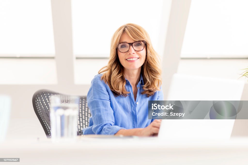 Attractive mature using laptop while sitting at desk at home Portrait of happy businesswoman working on computer while sitting at desk. Home office. Women Stock Photo