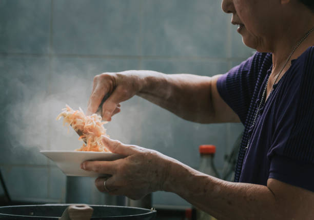 アジアの中国人の先輩女性が食事を準備し、台所で食べ物のカブを調理する - senior adult women adult tan ストックフォトと画像