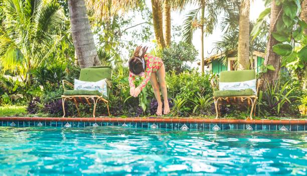 Girl in swimsuit dives into backyard pool in summer Little girl dives into backyard tropical summer pool vacation rental mask stock pictures, royalty-free photos & images
