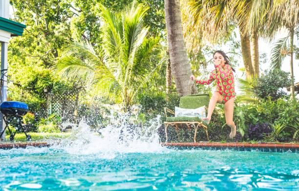 Girl in swimsuit jumps into backyard pool in summer Kid dives into backyard tropical summer pool vacation rental mask stock pictures, royalty-free photos & images