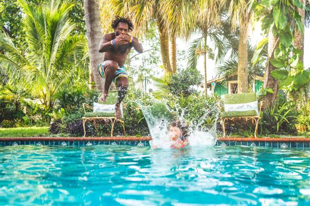 istock Man and child splash playfully into tropical backyard pool 1271151948