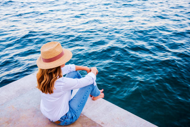istock Relaxed woman sitting on cliff and watching the blue ocean 1271153075