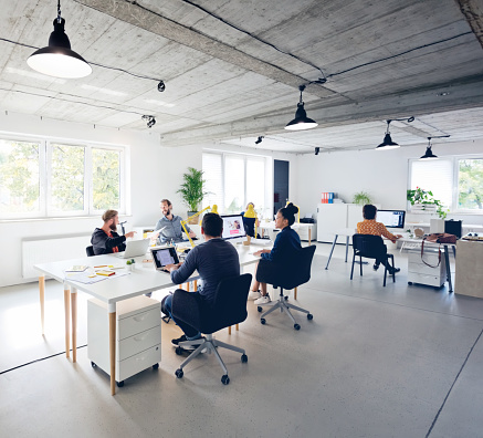 Male and female professionals working in new office. Business executives are discussing while sitting by desk at creative workplace. They are in casuals.