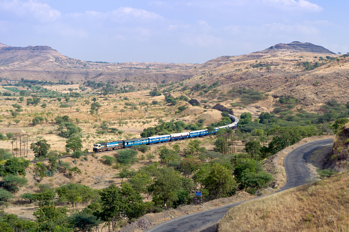 Train passing on a curved track with background of hills and sky and a foreground road.