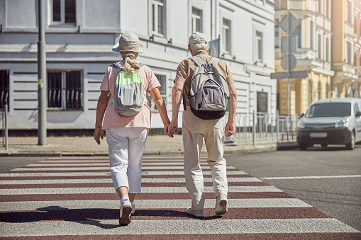 Back view of two modern senior Caucasian tourists crossing the street in the city center
