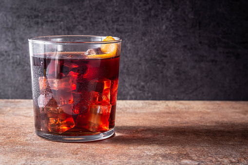 Boulevardier cocktail and orange zest on wooden table.